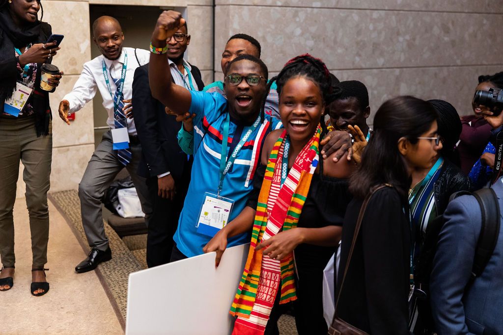  Male wearing blue shirt has a fist bump as he smiles while standing with Barbara Agyapong (female from Ghana) who is the founder of BidiGreen. She won first place. Both male and female are smiling.