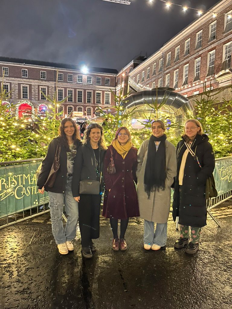 McKenzie and friends posing in front of Christmas trees at a local maket in the evening