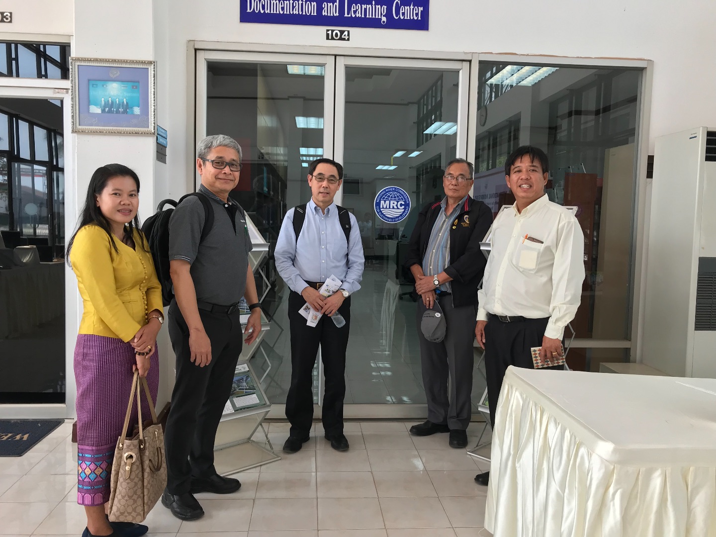 Dr. Qi poses with four colleagues from Southeast Asia outside of a room with glass sliding doors.