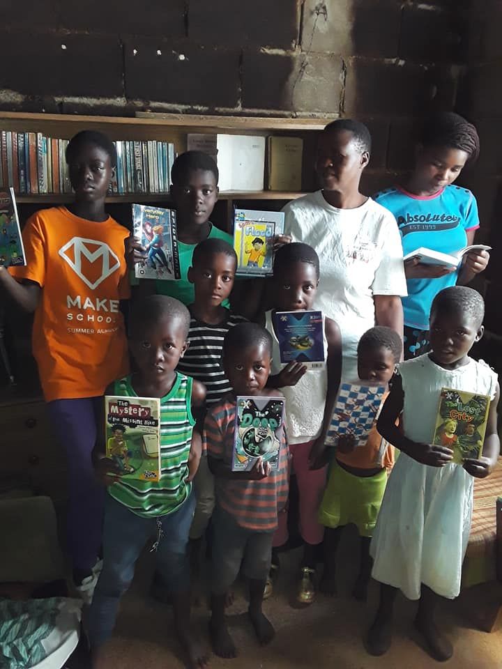 A group of eight youth in Zimbabwe stand together posing with books