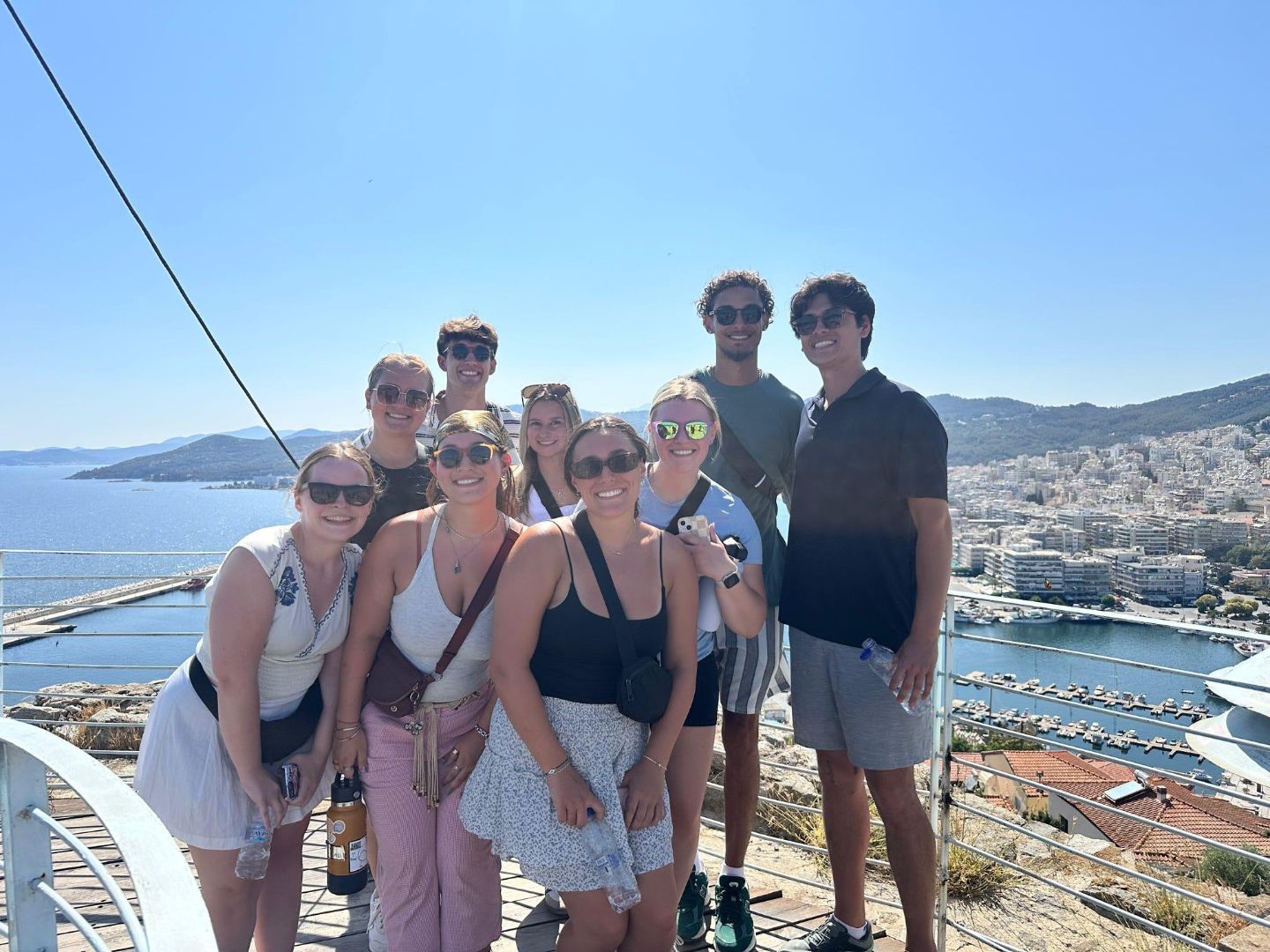 Ava and friends pose on a balcony overlooking the sea in greece