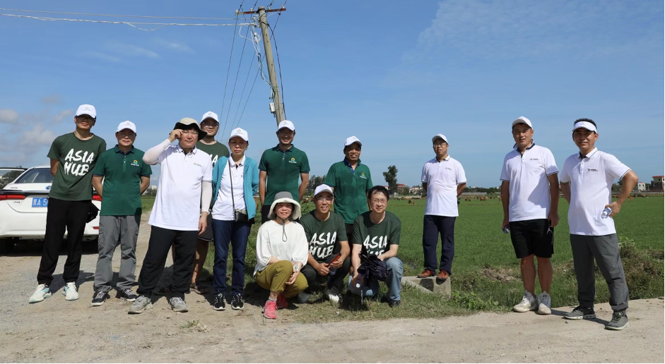 Several scientists gather around Qi, kneeling, in front of a large green field with brilliant blue skies.