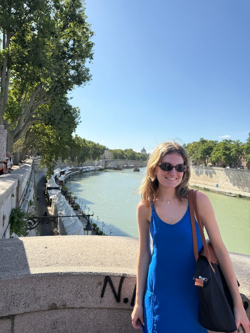 Kaci wearing a bright blue tank top and sunglasses standing on a bridge over the Tiber River in Rome