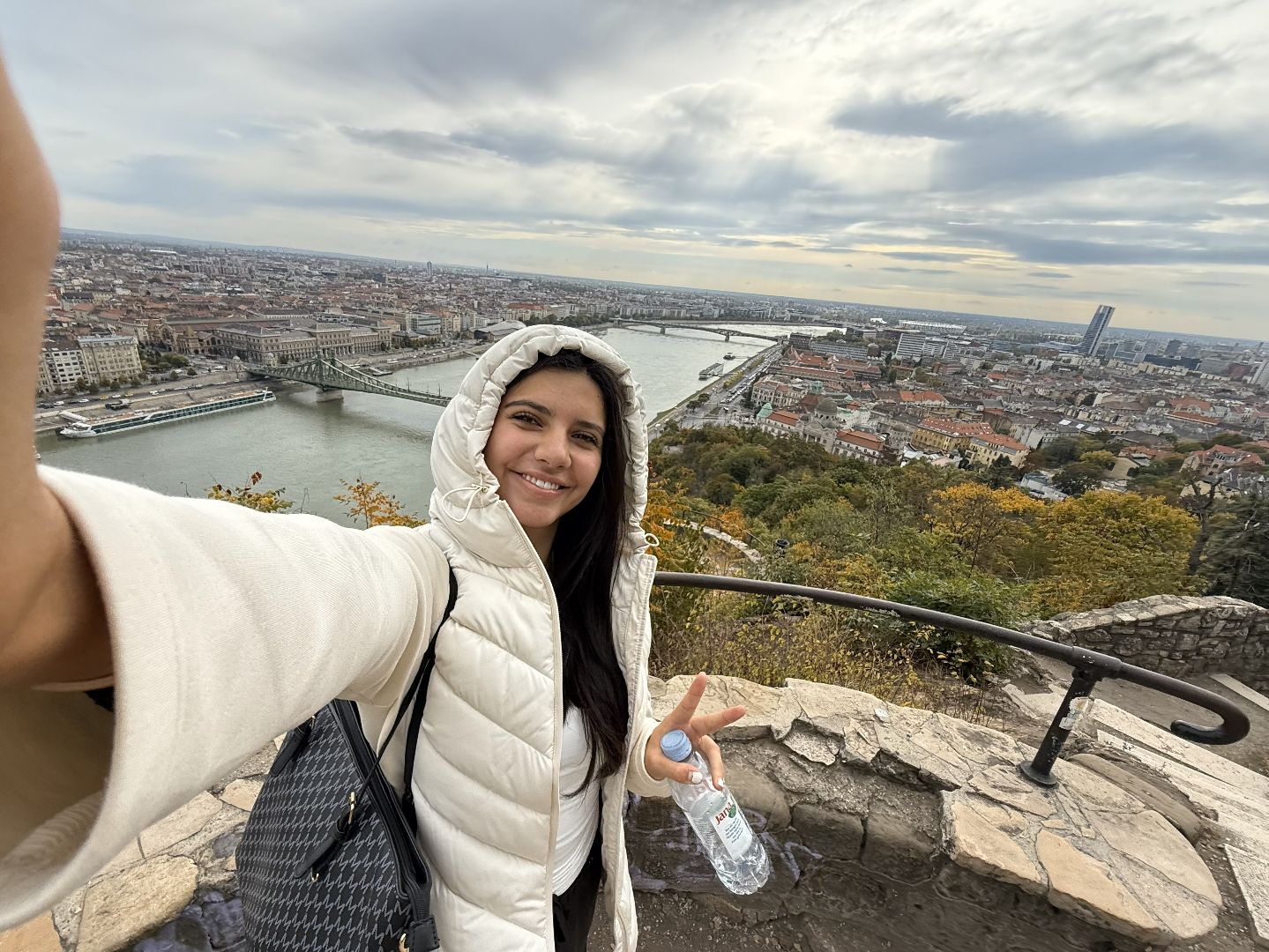 Fili wearing a white coat with a hood taking a photo of a river on top of a castle in Italy