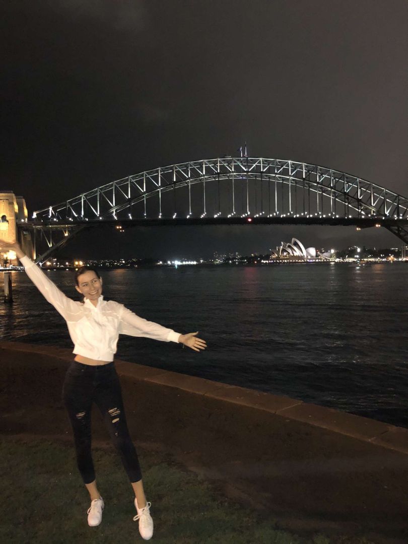 Katarina with arms up at night by Sydney Harbor Bridge in Australia
