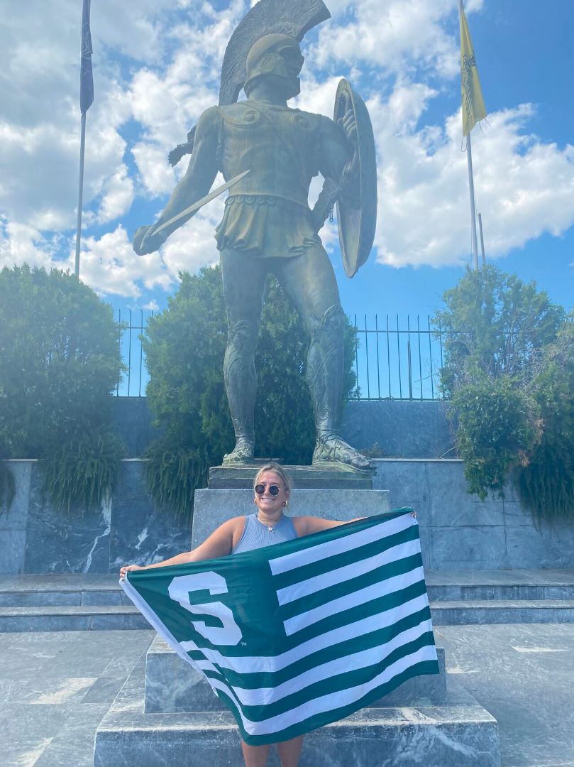 Sofia holding Spartan flag in front of Spartan statue in Greece
