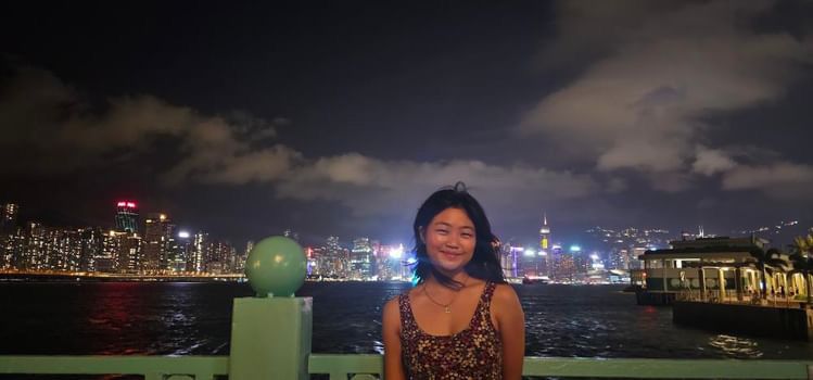 Katrina posing for a photo at night with the Hong Kong skyline behind her