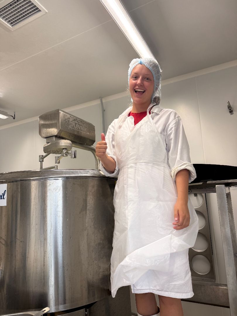 Lacey wearing a white apron and blue hairnet inside a cheese factory