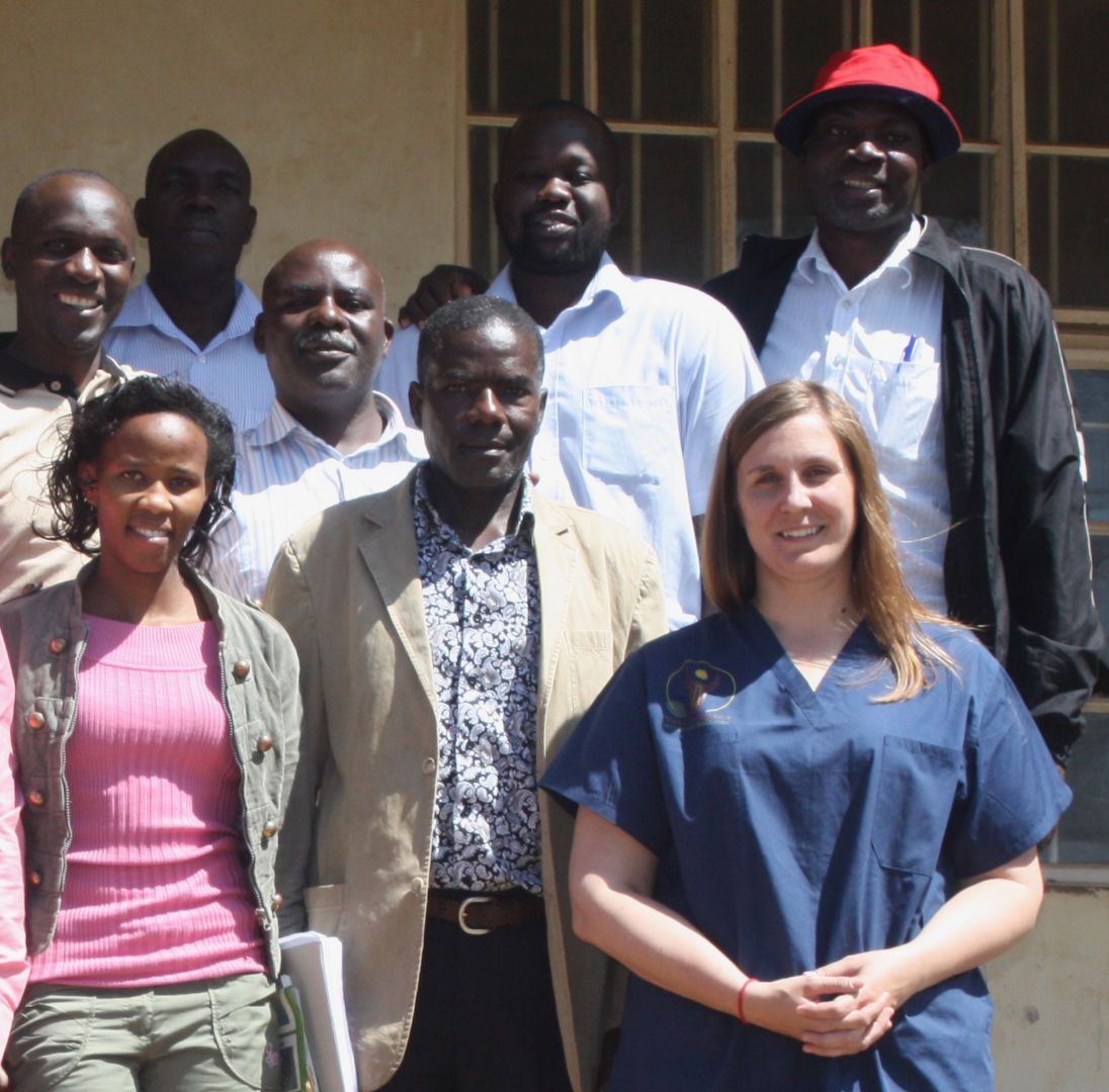 Sarah stands smiling with seven of her Ugandan colleagues on a bright sunny day.