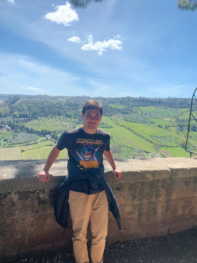 Nicholas standing by stone wall overlooking Italian countryside