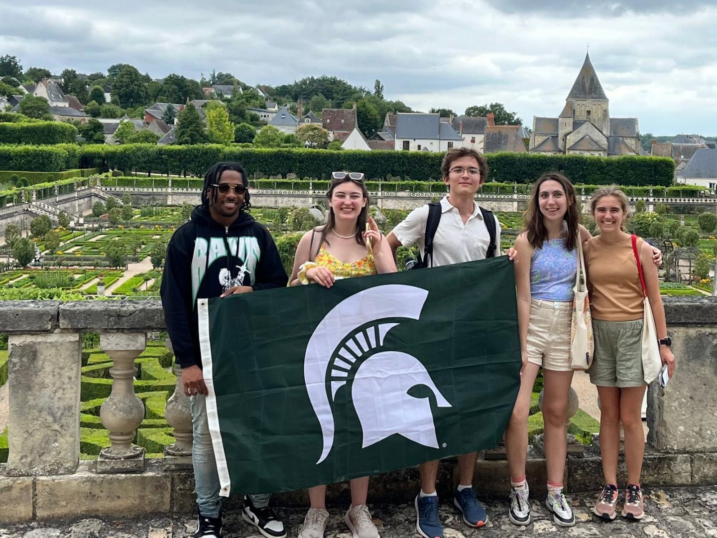 Joe with other students holding the Spartan flag in a garden in France