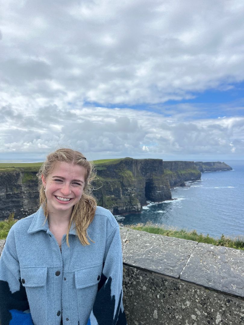 Katie wearing a blue shirt by the Cliffs of Moher in Ireland