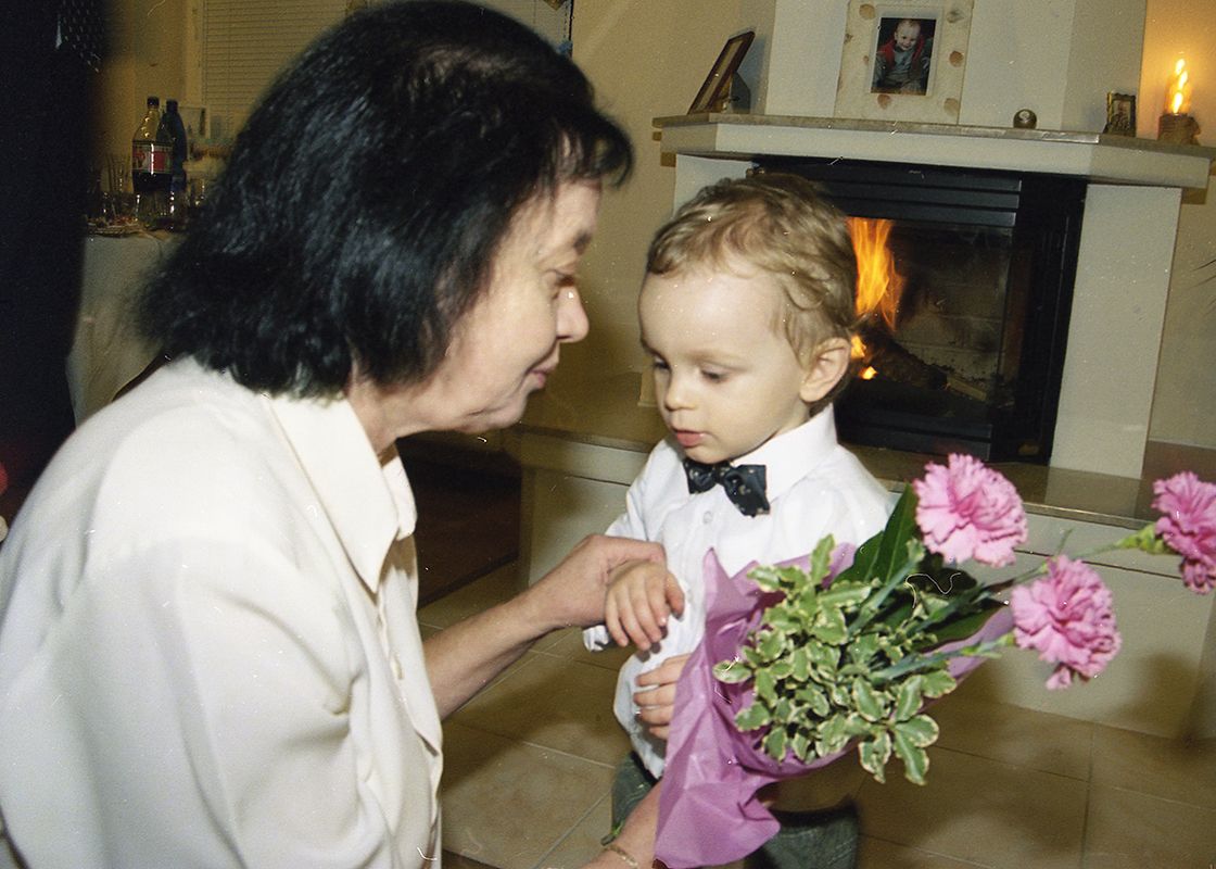 An elderly woman places a bouquet of flowers in the arms of her small grandchild.