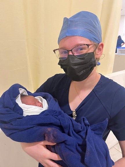 Ayla holding a baby while wearing medical scrubs