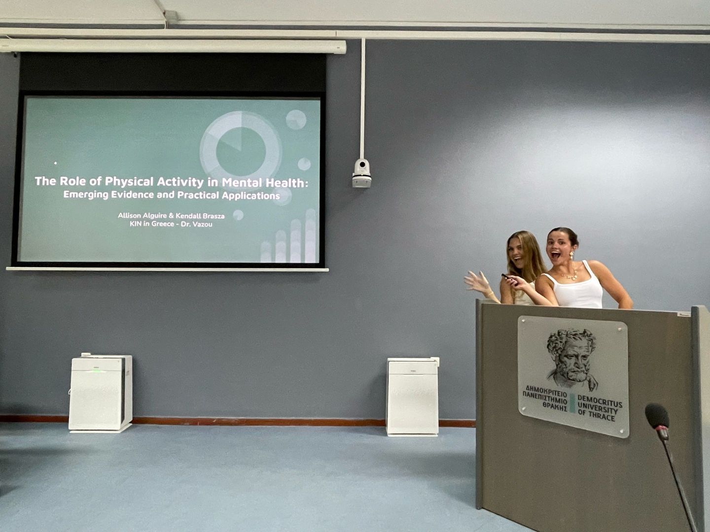 Kenall and classmate at a podium with a PowerPoint slide on a screen that reads the Role of Physical Activity in Mental Health