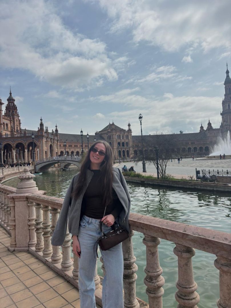 Annika wearing sunglasses, jeans, black shirt and grey coat standing next to a canal in Spain