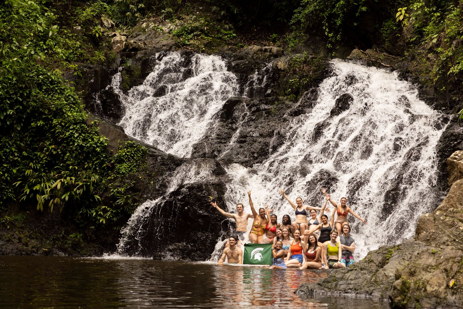 Group of students with Spartan Flag at the base of a waterfall