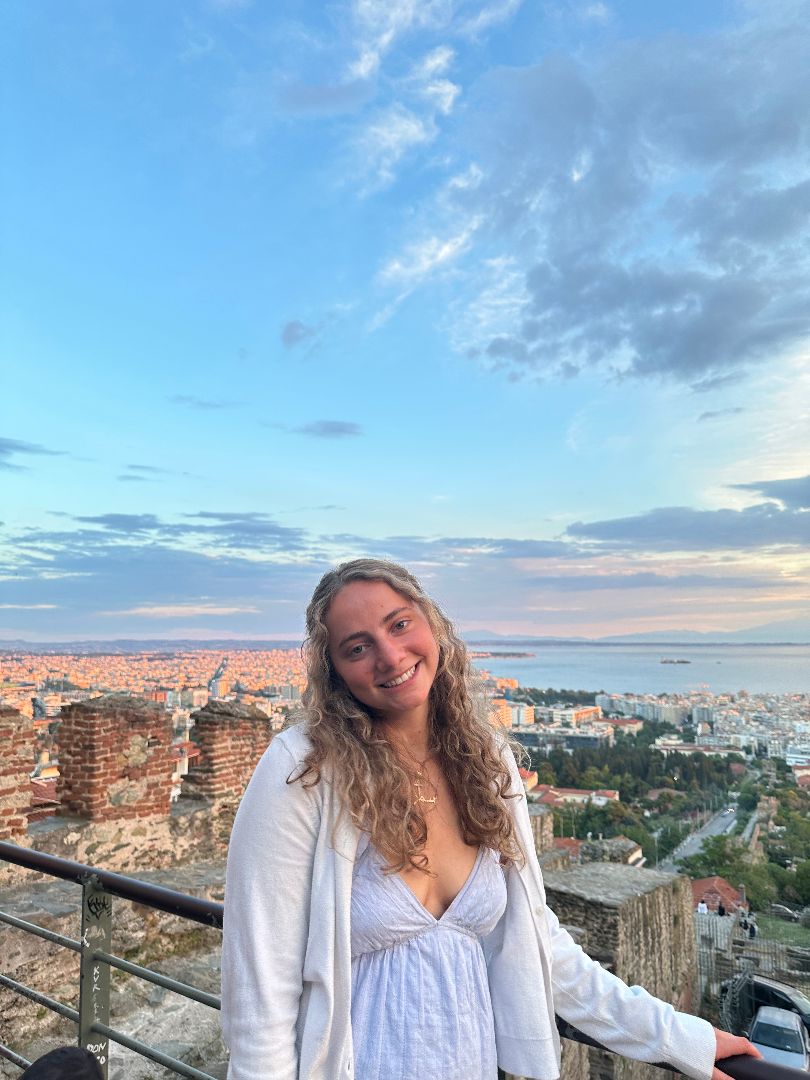 Sommer wearing a white dress standing on a rooftop overlooking a European city