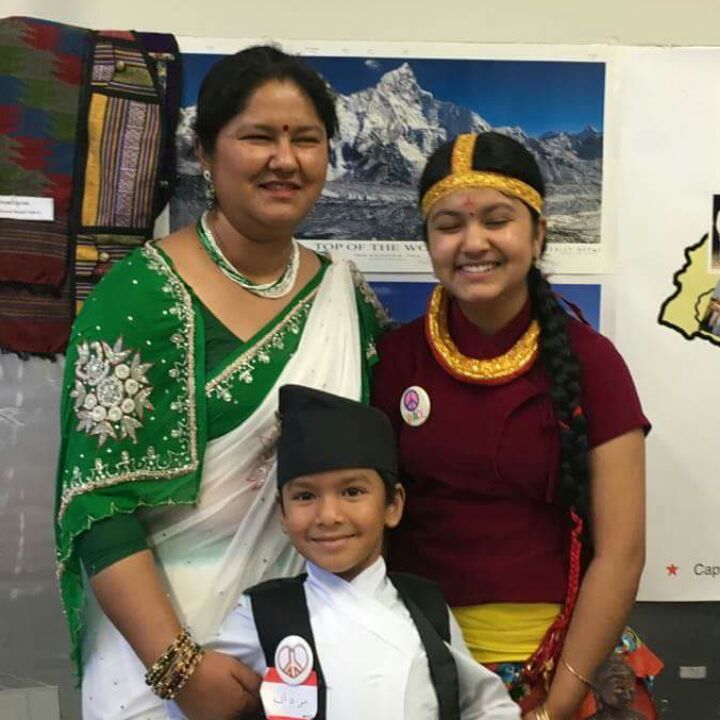 A woman and her two young children smile for the camera dressed in traditional Nepalese clothing. 