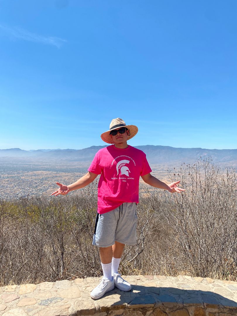 Yosmar wearing a pink MSU shirt standing atop a mountain in Mexico
