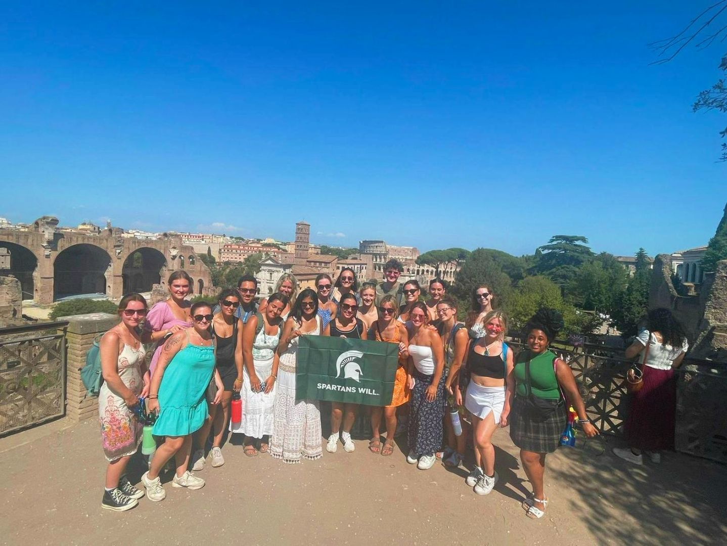 Group of students holding the Spartan flag with the cityscape of Rome in the background