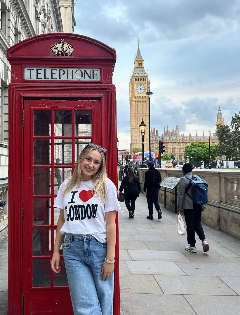 Hailey wearing an I love London tee shirt standing next to an iconic red phone booth