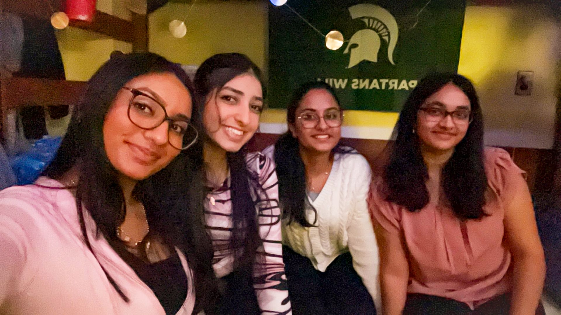 Navya posing with friends in front of an MSU banner