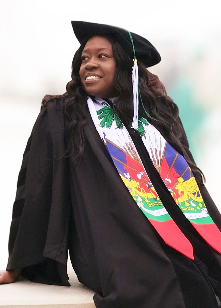 woman with graduation cap and gown. She is facing camera and smiling.