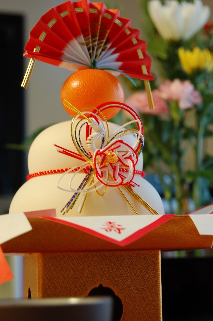 two mochi topped with a citrus fruit and a paper fan