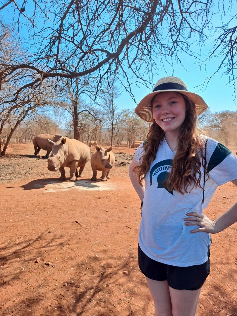 Andrea wearing a Spartan shirt standing in front of 3 rhinos in South Africa