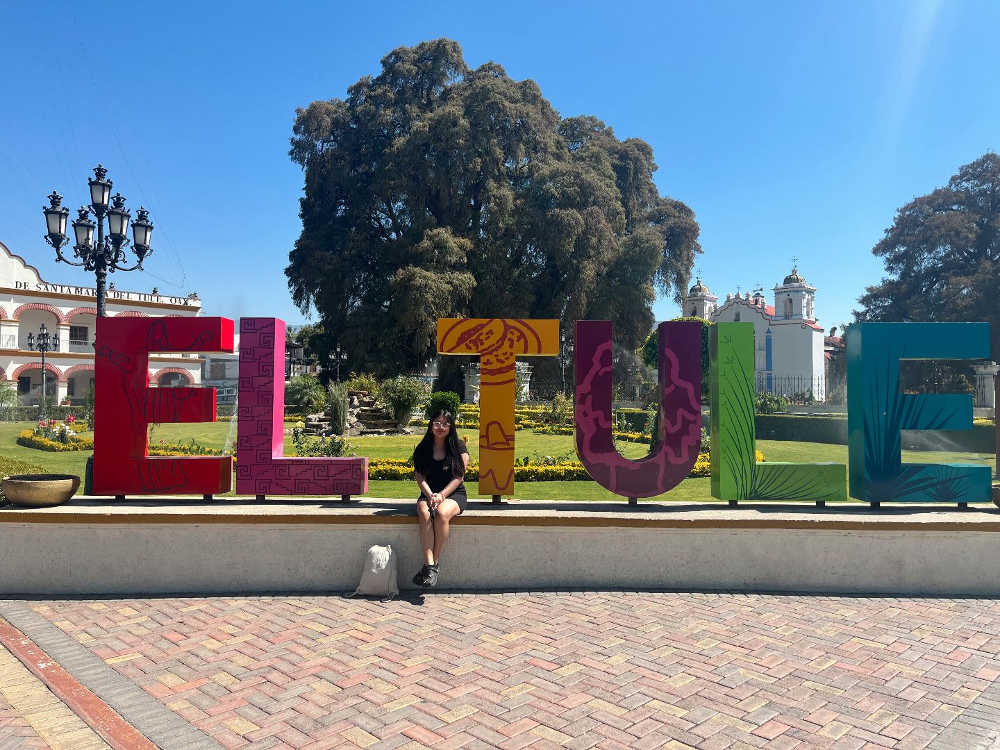 Jennifer sitting in front of a colorful El Tule sign in Mexico