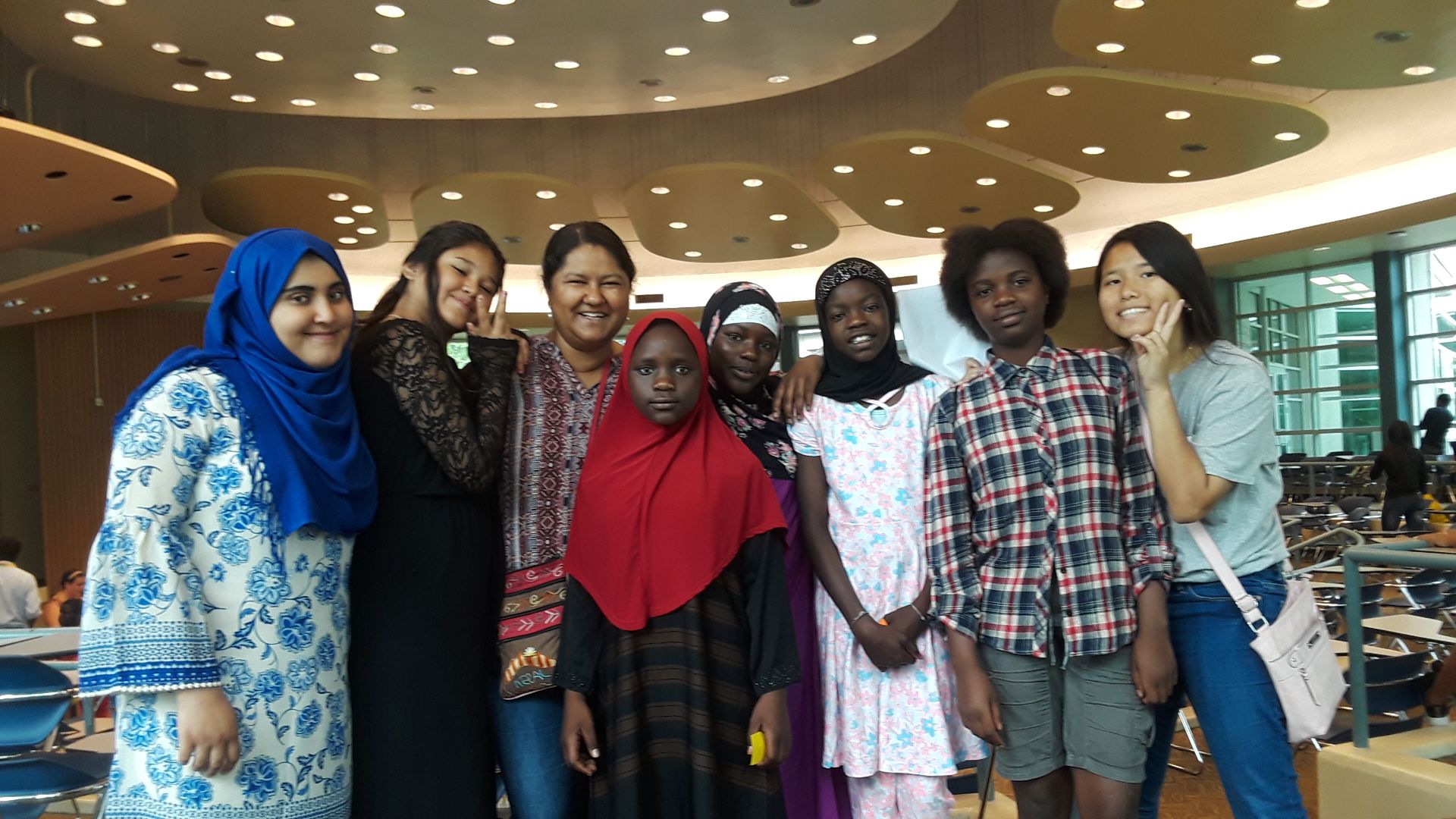 A multicultural group of smiling people posing for the camera, some are flashing peace signs.