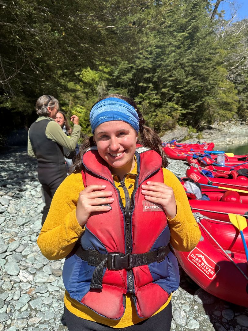 Nicole wearing a red life jacket standing on rocky shore of New Zealand