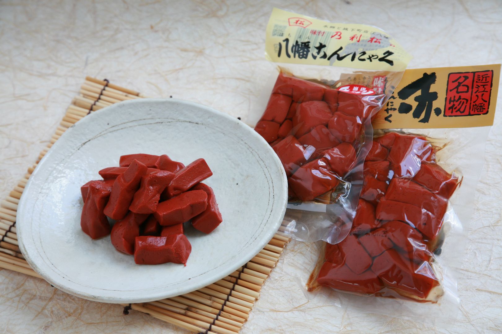 A plate of red konnyaku, with two bags of red konnyaku to the side