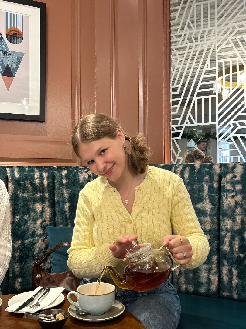 Iris wearing a yellow sweater pouring a cup of tea