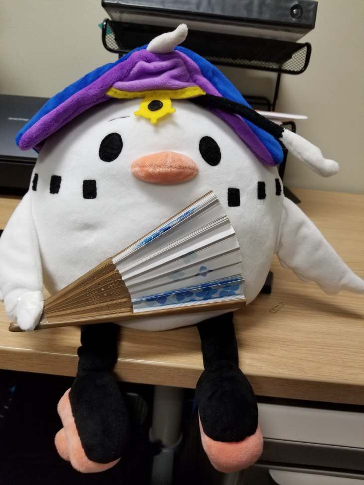 a stuffed toy swan sitting on a desk holding a Japanese fan