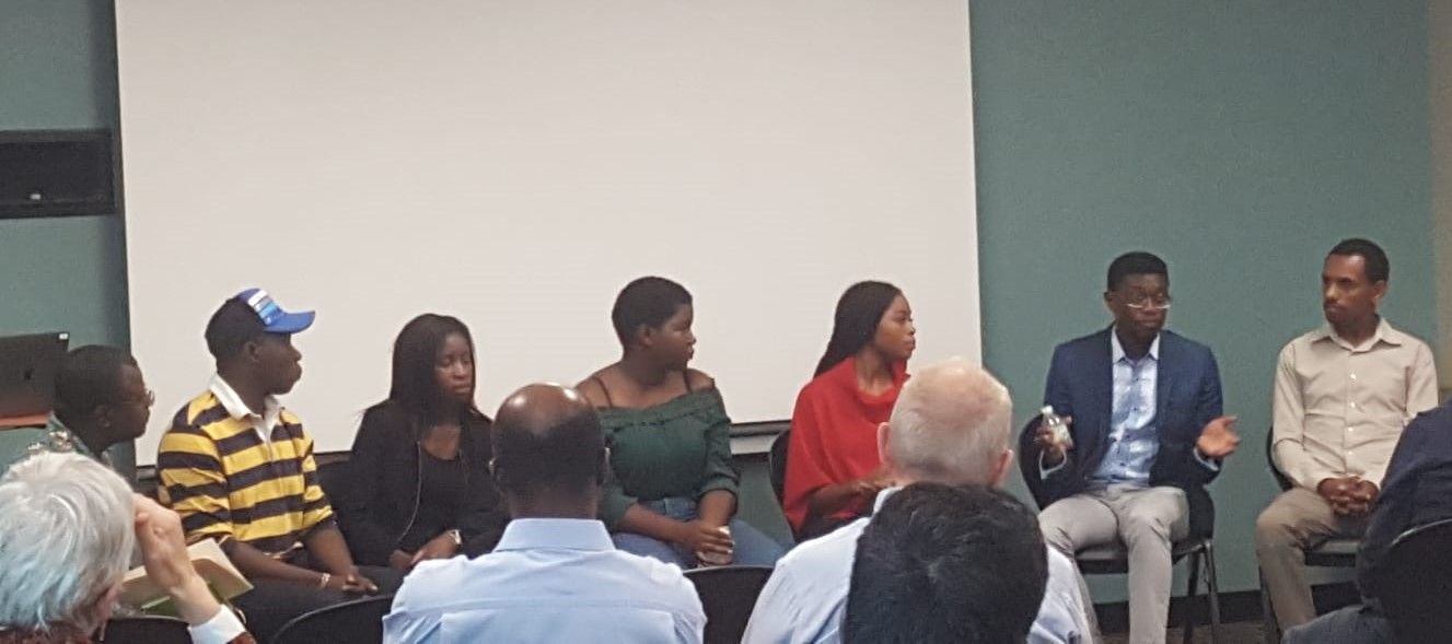 Six students from the Mastercard Foundation Scholars Program sit on a panel in the front of a room.