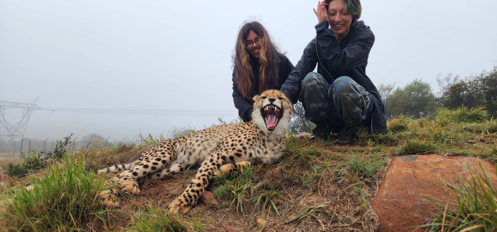 Elena knelling down with another woman and a cheetah with its mouth open in South Africa