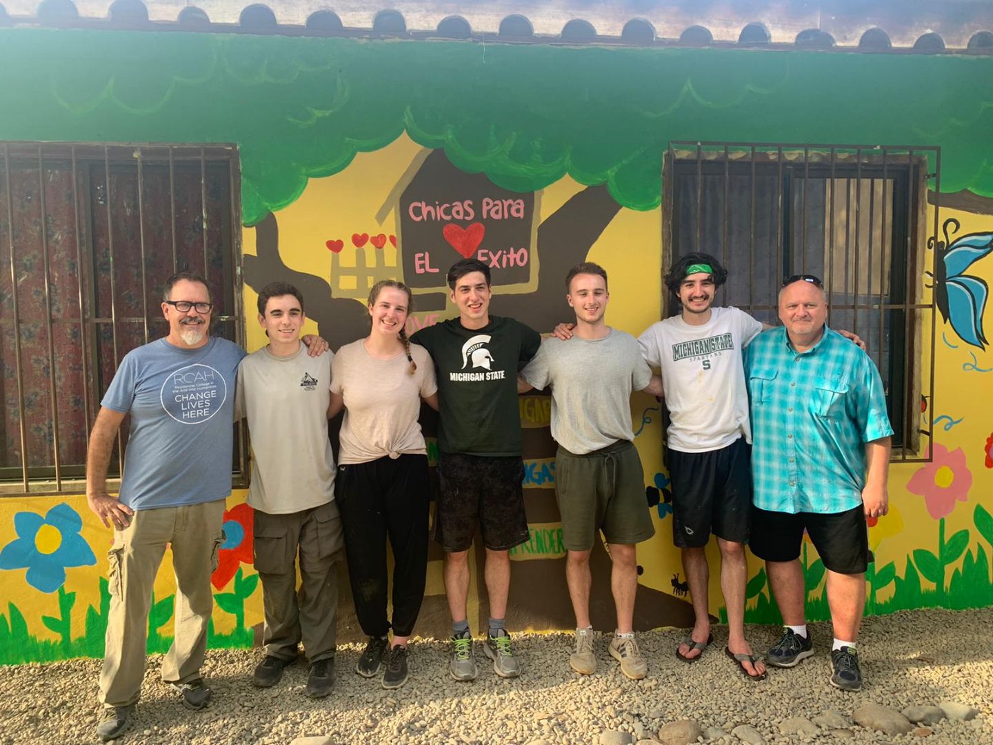 Delgad stands in front of a yellow painted wall with study abroad participants.