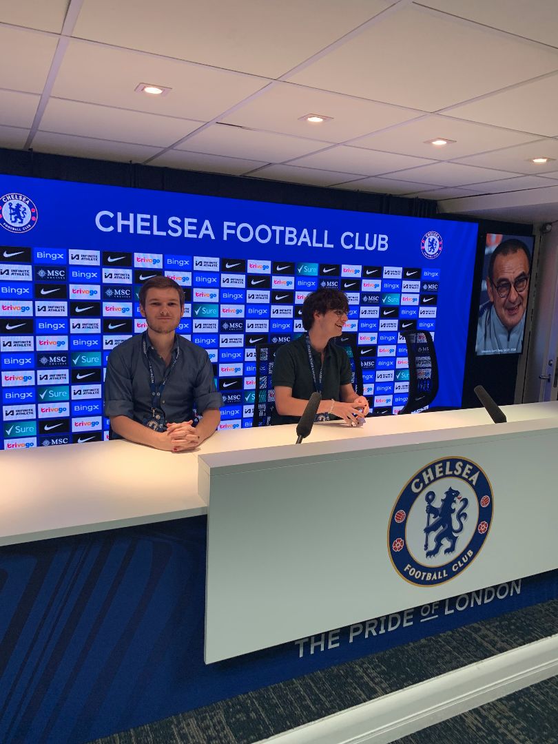 Noah and friend sitting behind broadcast booth at the Chelsea Football Club