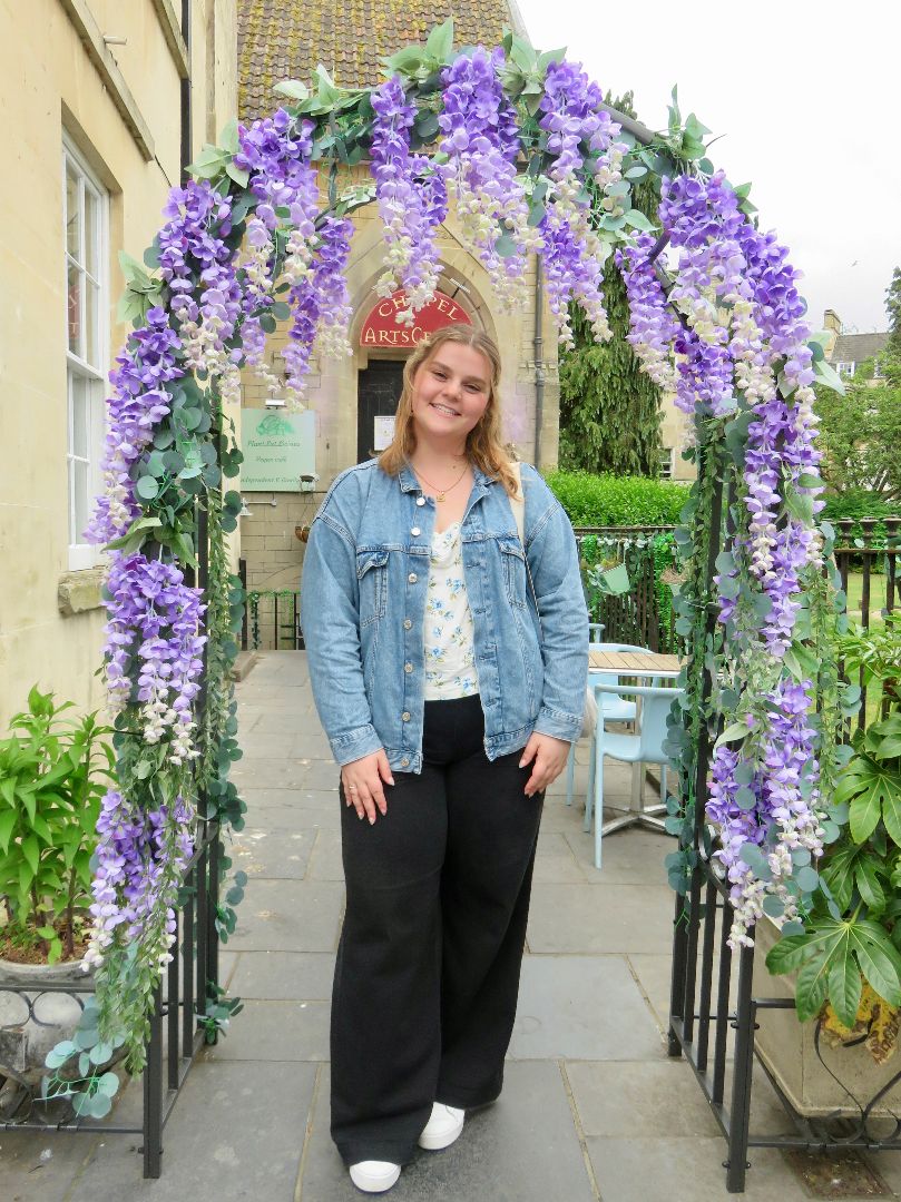 Edona standing underneath an arch of purple wisteria vines