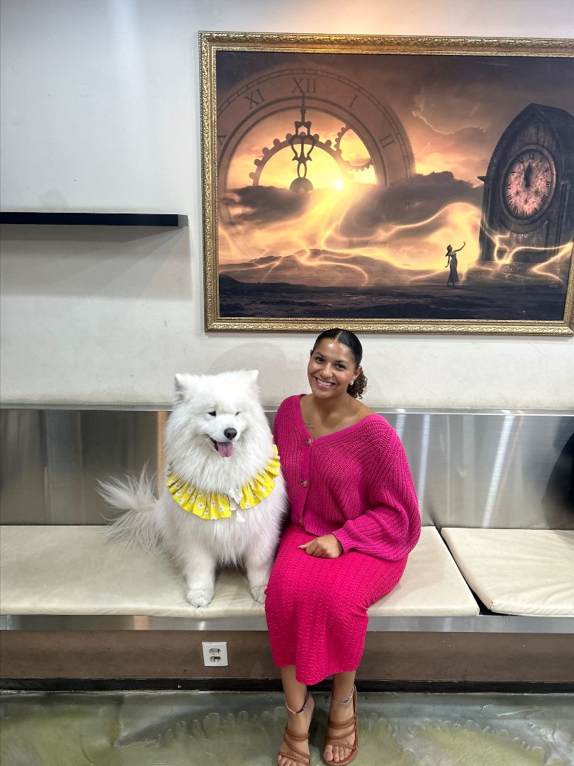 Marissa wearing a pink dress sitting next to a white dog