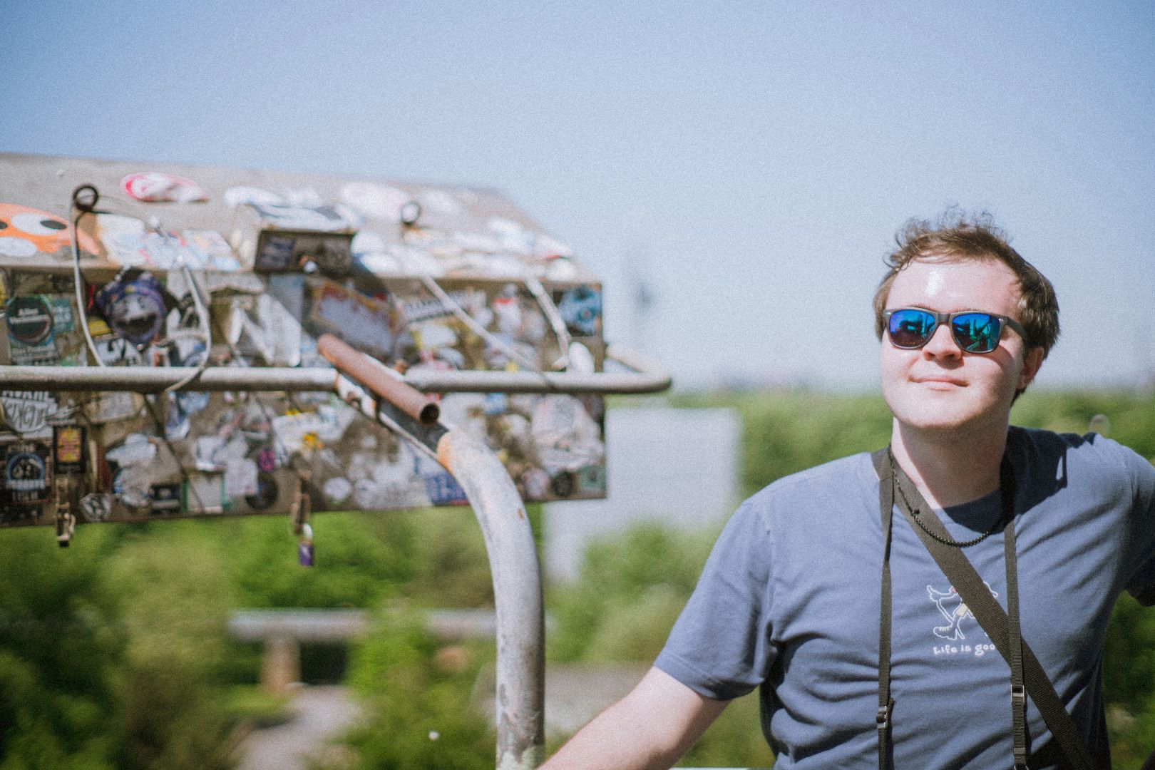 Cole wearing sunglasses posing near a metal object covered in stickers in Europe