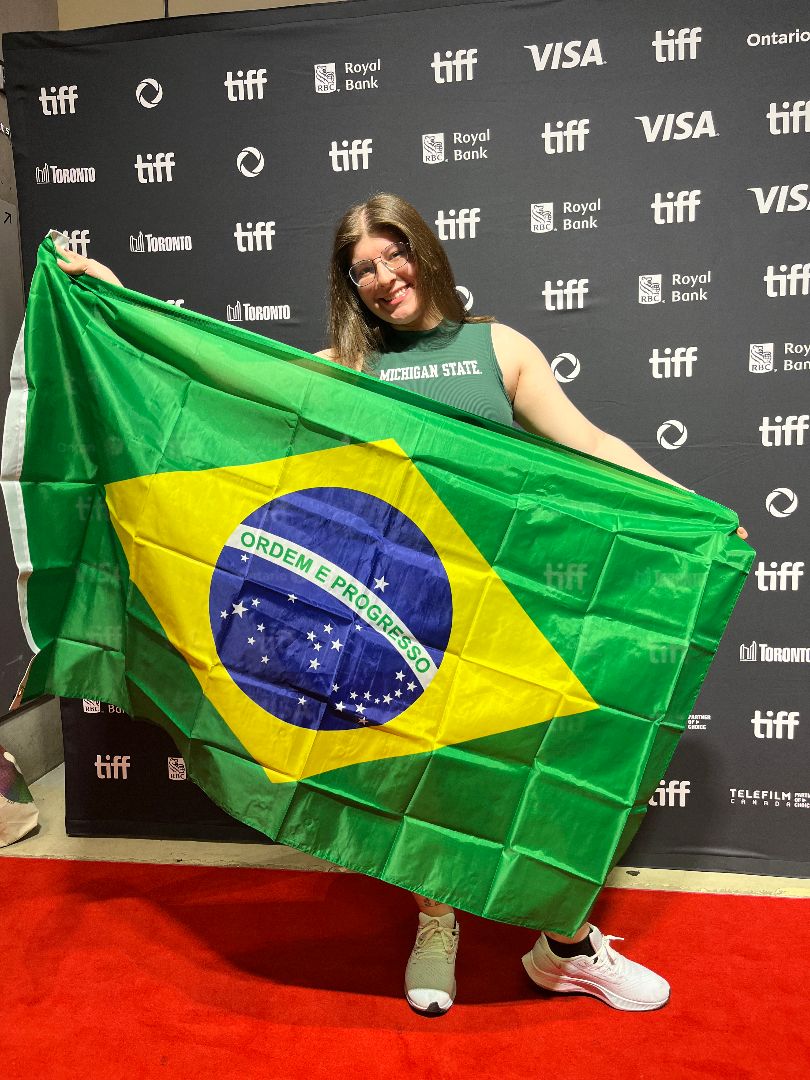 Yasmin holding a Brazilian flag in front of a TIFF backdrop