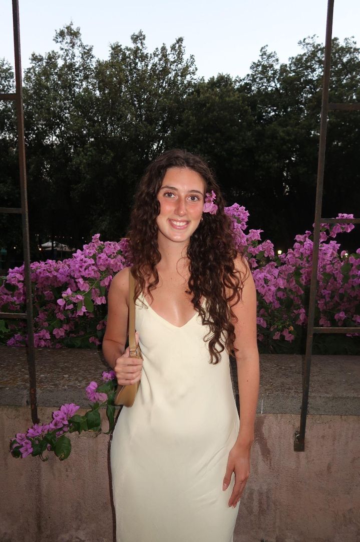 Nicole in a white dress with a purple flower in her hair standing in front of bushes of purple flowers