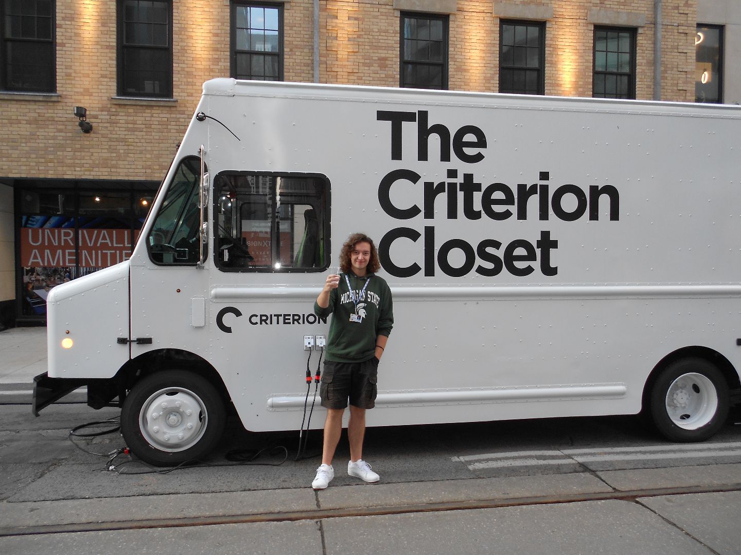 Jonathan wearing an MSU shirt standing in front of a white van that says The Criterion Closet
