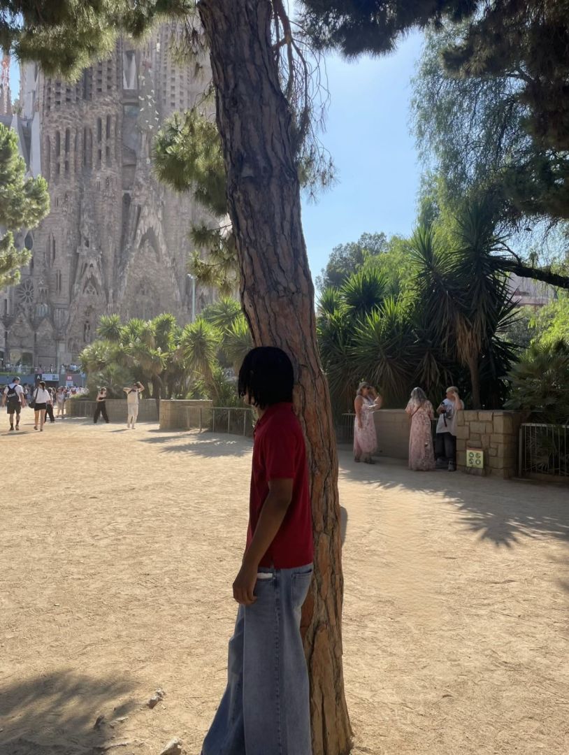 Zaviah wearing a red shirt leaning on a tree in Spain