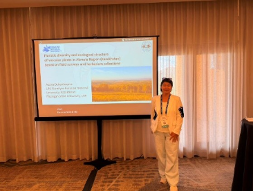 Dukenbayeva stands beside a presentation screen at a conference, giving a presentation on plant-related research.