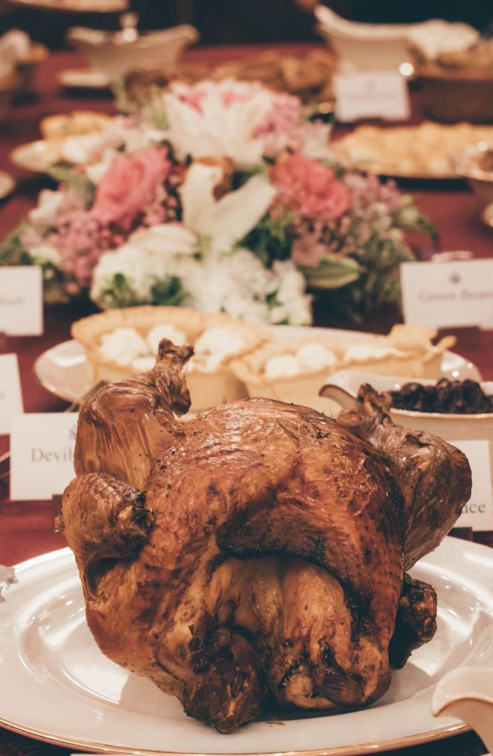 Close up of the roasted turkey before it is carved, with other dishes out of focus in the background.