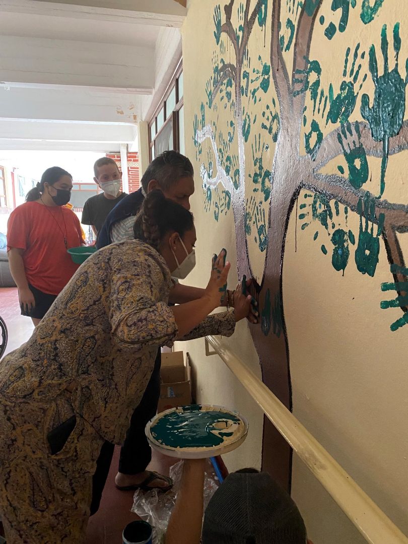 Alexie placing her painted hand a wall mural of a tree